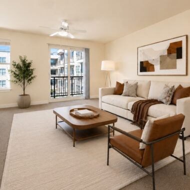 Sun-lit apartment living room with balcony access and carpet, decorated with contemporary furniture and decor in browns and neutrals.